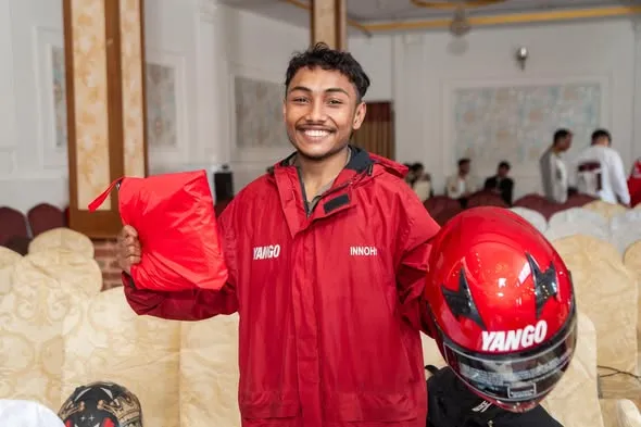 Smiling Yango rider holding a red InnoHub jacket and helmet